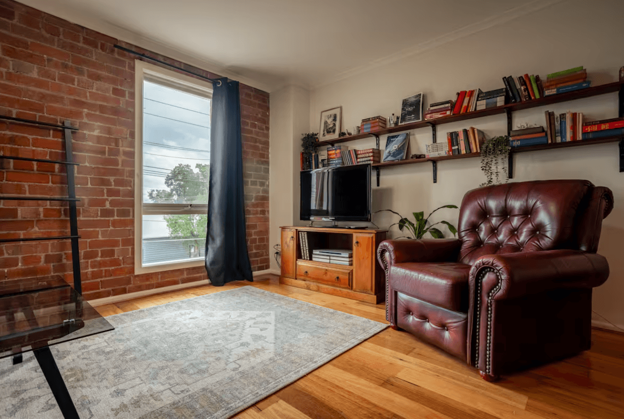 The living room of the Brickworks Heritage Loft in Brunswick, with exposed brick, timber floors and shelves of books